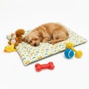 Cachorro peludo deitado no colchonete estampa de carrinhos da Loli e mel, com alguns brinquedos ao redor.